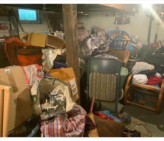 A basement of a home loaded with contents and debris in many piles and hiding sewage damage