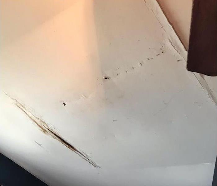 A white bedroom ceiling bulging and breaking from water damage