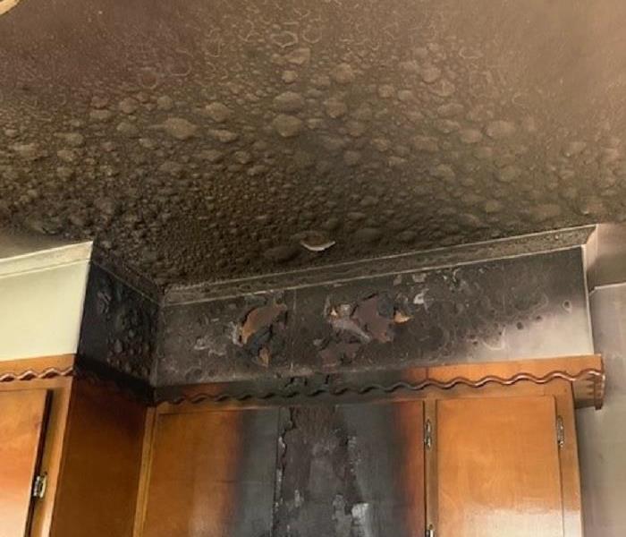 A charred and burned oven hood, ceiling and cabinets above the stove in a home