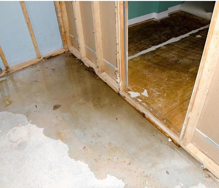 A large and extended puddle of water covering areas of an unfinished basement floor.