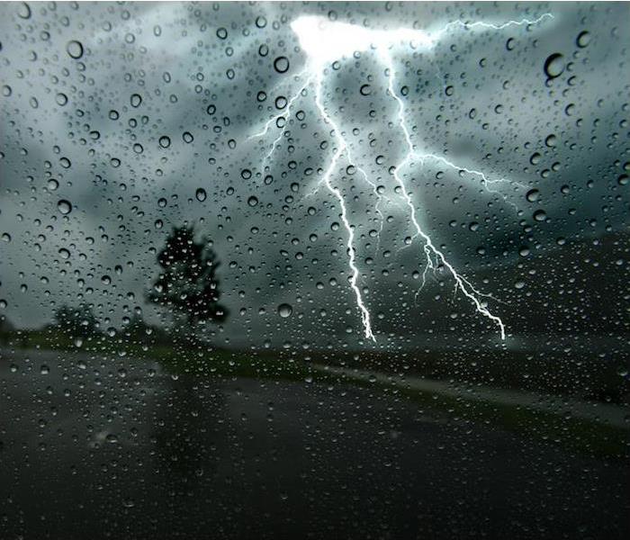 A rain pelted window-view of a black sky and a huge bolt of white lightning.