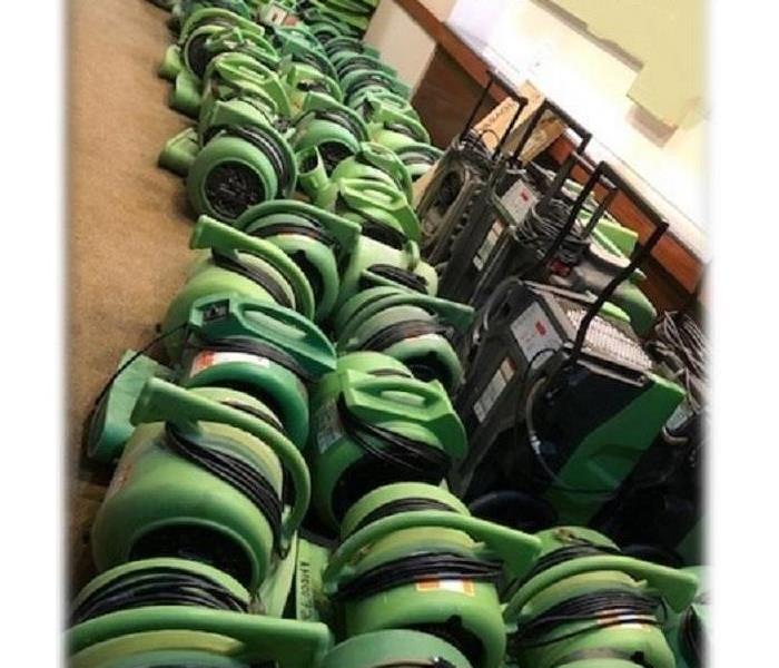 Tons of SERVPRO green equipment lined up against the wall of a commercial building.