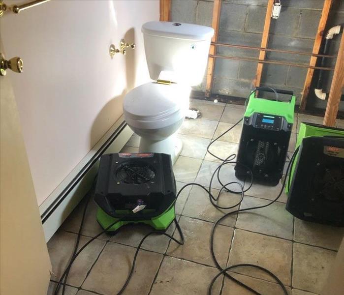 A bathroom with the walls and appliances removed and green drying equipment placed throughout.