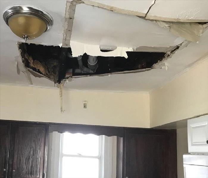 A large tear, split and hole in a kitchen ceiling from water damage in a burst pipe above.