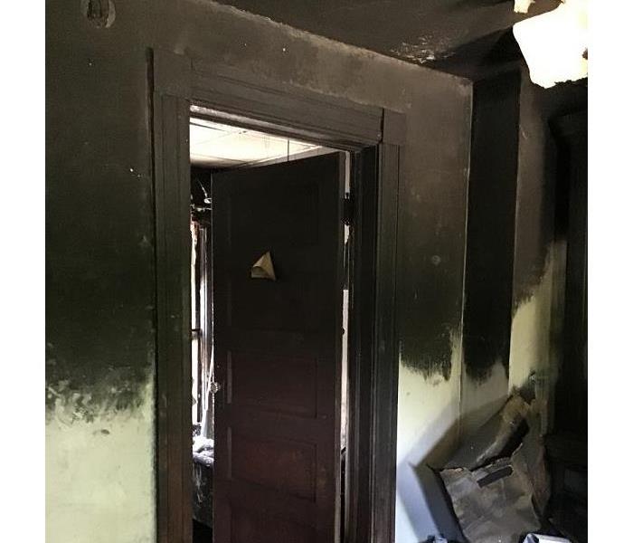 The doorway of a bedroom with blackened walls and a charred frame with damage up to the ceiling