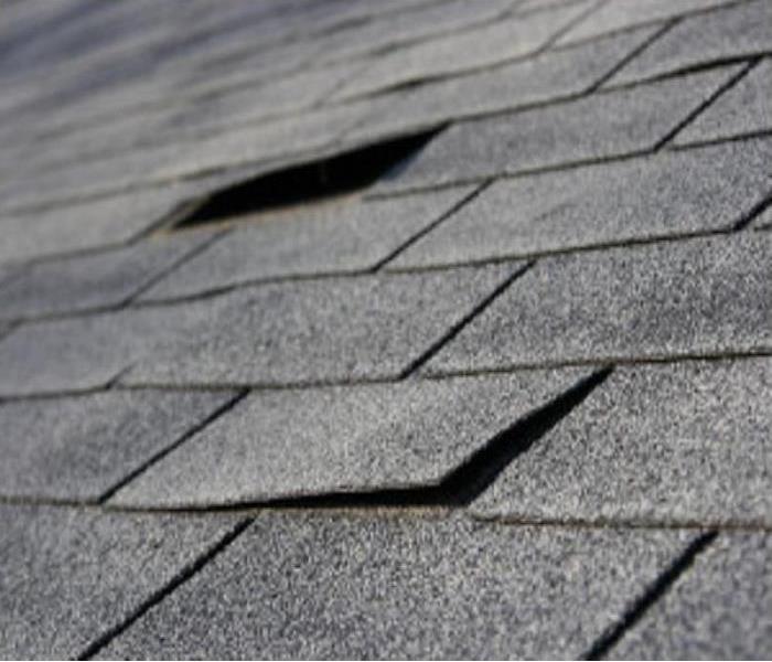 A section of a gray roof of a home with 2 damaged shingles