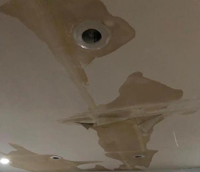 A living room ceiling with large patches of water staining around a recessed light.