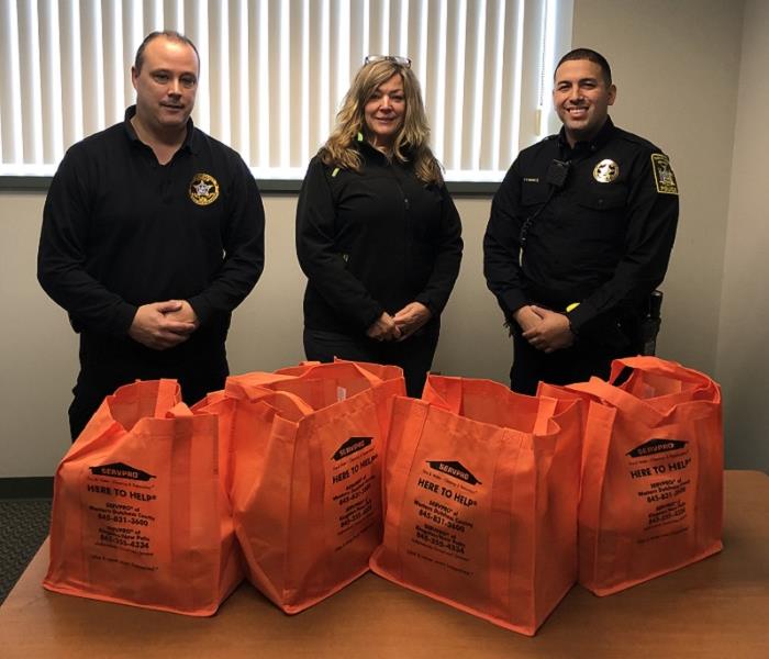 A photo of 3 people surrounded by orange bags of donated food items